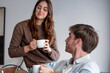 © luciano - Young heterosexual couple sits on a sofa, drinking coffee and chatting, enjoying indoor time together