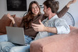 © luciano - Happy young couple relaxing on sofa with laptop at home, watching content and having fun together