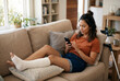 © Meow Creations - Woman with broken leg in cast relaxing on couch using smartphone