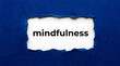 © NUR - Torn blue paper reveals the word mindfulness in black text ripped white