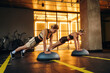 © standret - Two women performing push-ups on balance trainers in a modern gym with bright lighting and exercise equipment visible in the background