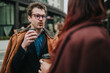© qunica.com - A young man and woman chat while holding takeaway coffee during a winter business meeting. The candid outdoor conversation captures colleagues speaking on an urban street.