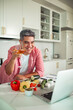 © Marko Geber - Smiling man toasting with wine on a video call in home kitchen