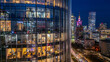 © AmazingAerialAgency - Aerial view of the illuminated glass facade of a modern skyscraper with office interiors and the Warsaw city skyline featuring the Palace of Culture and Science at night in Poland.