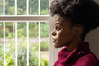 © Wavebreak Media - African adult woman gazing out white window with vertical bars in maroon ribbed sweater, copy space
