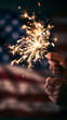 © Olga Ко - Hands holding a burning sparkler against a blurred American flag background. Patriotic 4th of July Independence day celebration concept