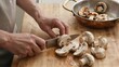 © joeycheung - Person slicing mushrooms on wooden board near copper pan with sauteed pieces.