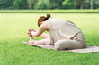 © buritora - A woman stretches, warms up, and bends forward on the grass in a park.