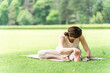 © buritora - A woman stretches, warms up, and bends forward on the grass in a park.