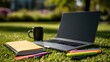 © Oulaphone - Laptop, notebook, pens, and coffee cup placed on grass in a sunlit outdoor setting, suggesting a calm and productive workspace in nature.