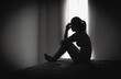 © Tinnakorn - Depressed woman sitting alone in a dark room, representing domestic violence, emotional abuse, trauma, anxiety, loneliness, fear, and mental health struggles.