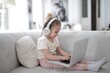 © Cavan Images - Young girl with headphones using a laptop on the couch