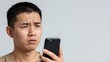 © Qazy - Confused asian man looking at smartphone with furrowed brow
