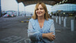 © Krakenimages.com - Middle age woman with hands visible, arms folded and in alternate frames points finger at airport terminal, wearing light blue blouse; confidence independence.
