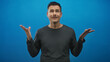© Krakenimages.com - Young hispanic man with moustache shrugging hands in studio against blue backdrop, wearing gray long sleeve shirt with eyes closed and playful face; uncertainty doubt bemused.
