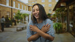 © Krakenimages.com - Young hispanic woman laughing with hands crossed over chest in a city street courtyard during daytime; joy celebration.