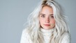 © svastix - A serene young woman with wavy hair appears contemplative and peaceful while wearing a cozy sweater. Her natural beauty shines against a calming grey background.