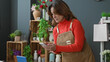 © Krakenimages.com - Woman florist in brown apron and orange sweater taps smartphone screen while arranging flowers and glancing at a tablet on a studio counter; concentration.