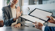 © Rayn - A businesswoman showing a stop hand gesture to reject a contract or document offered by a colleague at an office desk, representing business refusal and disagreement concept.