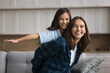© fizkes - Mother giving piggyback ride cute 10s daughter seated on couch, family enjoy funny active playtime together at home. Kid girl play with older sister in living room, laughing, having fun feel carefree