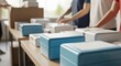 © Wong - Stacks of blue and white hygiene kits organized for distribution on a wooden table with hands preparing more supplies in the background.