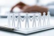 © Kowit - Paper cutout figures holding hands on clipboard with blurred hands typing on laptop in the background, symbolizing teamwork, unity, and collaboration.
