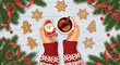 © Liam - Festive top view shows hands in a holiday sweater holding a Santa Claus gingerbread cookie and a warm cup of mulled wine with citrus.