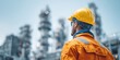 © Evgenii - Close-up of worker in orange uniform holding yellow hard hat and safety goggles at oil refinery. Concept of industrial safety, chemical engineering, manufacturing worker, and career in energy sector.