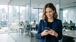 © Eve - Smiling young businesswoman texting on smartphone in glass office interior. Happy professional female entrepreneur using mobile app for corporate communication, checking online market data.