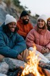 © Andrii Zastrozhnov - Group of friends sitting around a campfire on a rocky beach wearing winter jackets and beanies for outdoor lifestyle banner and cozy evening background