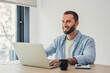© Daniel - Smiling young man with a beard concentrating on his laptop, working comfortably from his home office environment with a cup of coffee and notebook