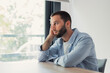 © Daniel - Young handsome man with beard looking away through a bright window, resting his head on his hand while contemplating, feeling worried, lonely, or thoughtful indoors