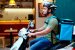 © DragonImages - Young adult Caucasian man riding scooter with insulated delivery backpack, working food courier shift for last mile service. Ideal for gig economy, app delivery, urban logistics marketing