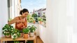 © Nina - Young woman watering potted plants on a sunny urban balcony garden, sustainable lifestyle and home gardening concept