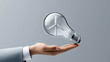© Achirawee - A conceptual image of a light bulb with a wind turbine inside, held by a businessperson, symbolizing the idea of investing in renewable energy. The background is minimalistic, allowing for ample copy