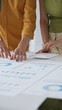 © rogerphoto - Two business professionals are collaborating on a project, analyzing financial charts and statistics displayed on a table, using a calculator for precise calculations. close up vertical view