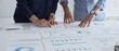 © rogerphoto - Professional team reviewing financial documents, pointing at charts on desk, collaborating to analyze data and strategize business growth. Business people concept
