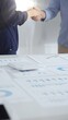 © rogerphoto - Businesspeople shaking hands over a conference table, finalizing a deal with financial documents and digital tools. Handshake concept