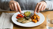 © Anthichada - A person uses a knife and fork to cut a grilled chicken breast served with avocado slices, cherry tomatoes, and sweet potatoes. Nutrition balanced, Healthy food concept