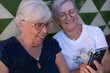 © luciano - Two senior women smiling and laughing, holding a smartphone, looking at its screen, enjoying a moment of connection and modern technology