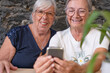 © luciano - Senior women friends are sharing a moment together, smiling and looking at a smartphone, actively enjoying digital connection and browsing content online