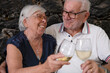 © luciano - Happy senior couple laughing and making a toast with white wine, celebrating their love and retirement during a special moment together outdoors