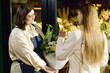 © TrueFrame Collective - Caucasian female florist presenting bouquet to young adult woman in flower shop, assisting purchase and discussing arrangement. Ideal for retail service, small business, gifting
