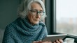 © progressman - Elderly woman uses digital device indoors