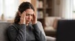 © TRIA - Tired young woman suffering from a headache sitting on sofa at home