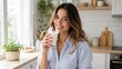 © Andrii  - Smiling young woman drinking a glass of milk in bright home kitchen