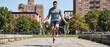 © Tromistudio  - Athletic man with muscular build performing jump rope cardio workout outdoors on a concrete path with city buildings and trees in the background on a sunny day focused on fitness