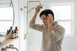 © Alexandra - Young asian man applying serum to scalp in modern white bathroom. Routine haircare and grooming for healthy hair growth. Wellness lifestyle concept for skin and body cosmetic treatment.
