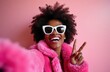 © miss irine - Black woman takes selfie in pink faux fur coat, white sunglasses, and big smile. She makes peace sign with fingers, showing happy, joyful, positive emotions. Fun, stylish, trendy look.