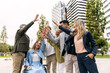 © Koldo_Studio - Diverse business people high fiving, celebrating teamwork, success, and inclusion in a city park with office buildings
